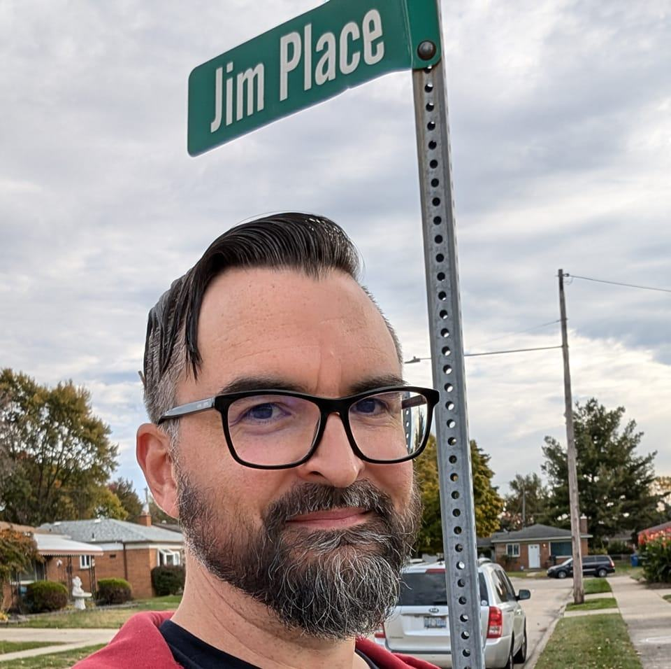 Jim McLuckie standing under a 'Jim Place' street sign in Ferndale